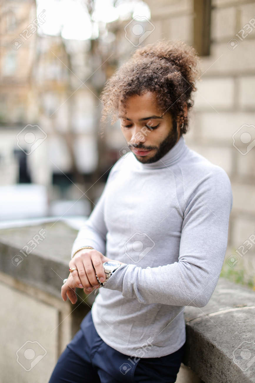 Black Male Person With Curly Hair Looking At Watch And Wearing