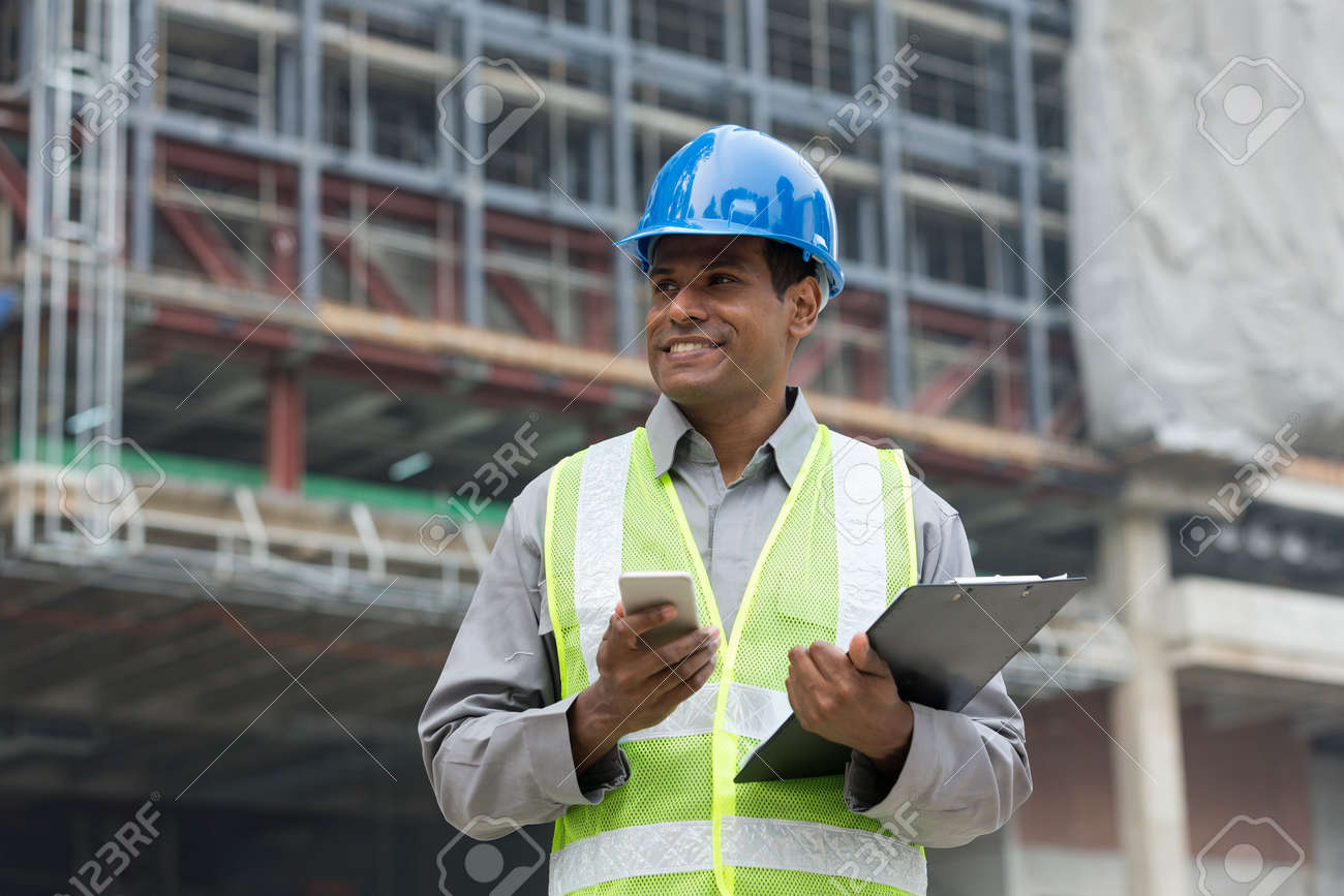 Portrait of a male Indian builder or industrial engineer at work using phone. - 54598372 Portrait of a male Indian builder or industrial engineer at work using phone. - 54598372