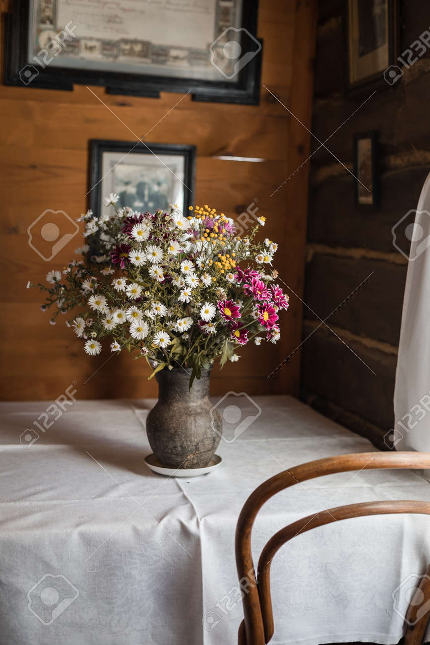 Old Clay Vase With Garden Flowers On The Table With A White Cloth - 
