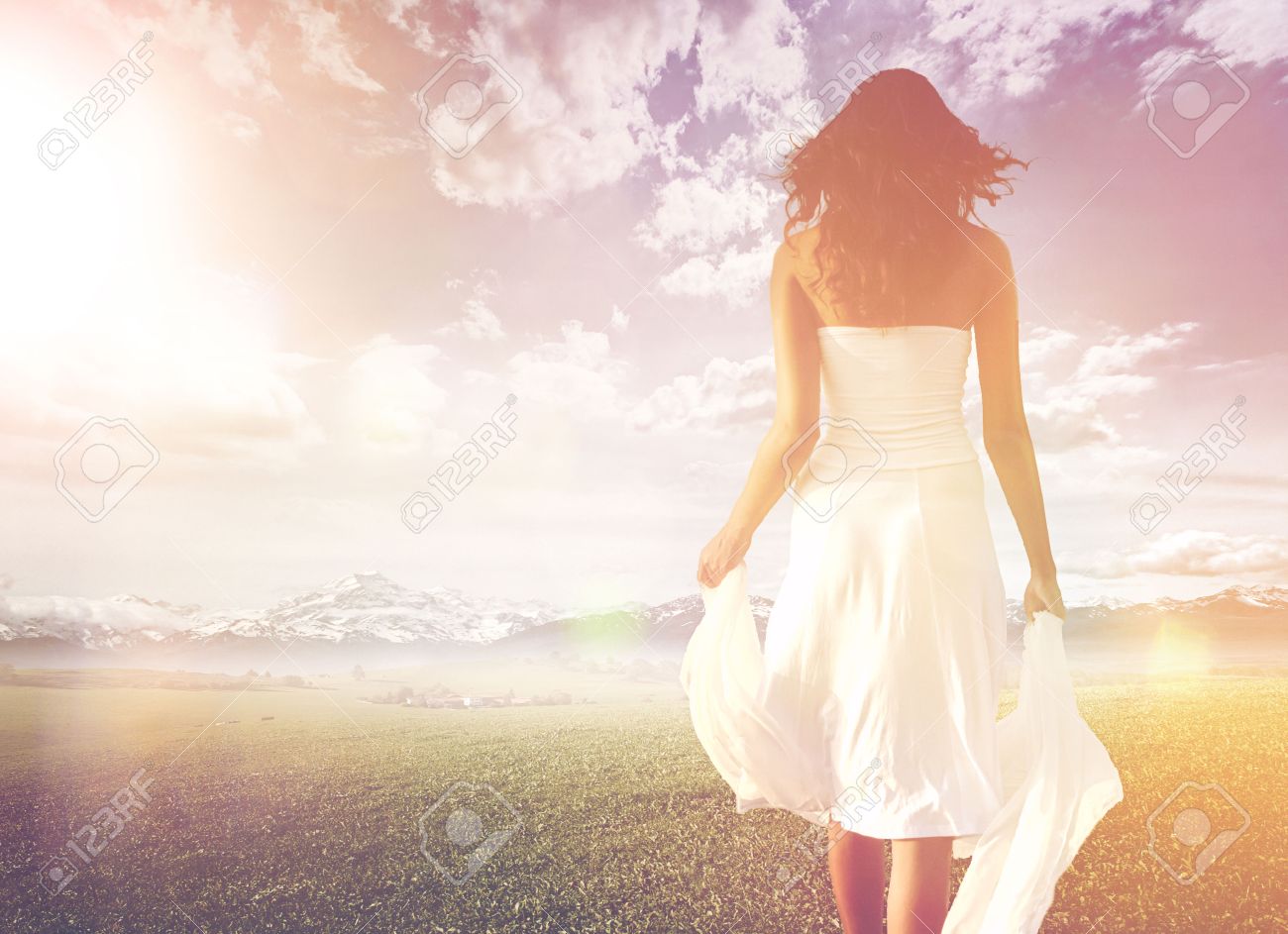 Slender long-haired woman wearing white summer dress while walking on a green meadow towards a bright and sunny horizon, under a dramatic sky, shot from behind, in high-key - 30007583 Slender long-haired woman wearing white summer dress while walking on a green meadow towards a bright and sunny horizon, under a dramatic sky, shot from behind, in high-key - 30007583