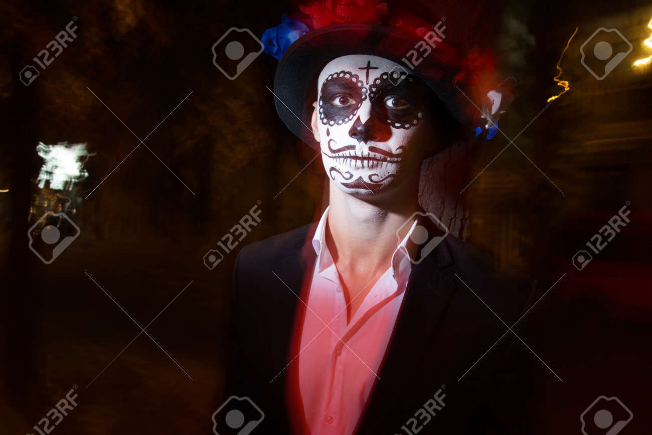A Man With A Painted Face Of A Skeleton, A Dead Zombie, In The City During The  Day. Day Of All Souls, Day Of The Dead, Halloween, Ghost Walk In A Hat