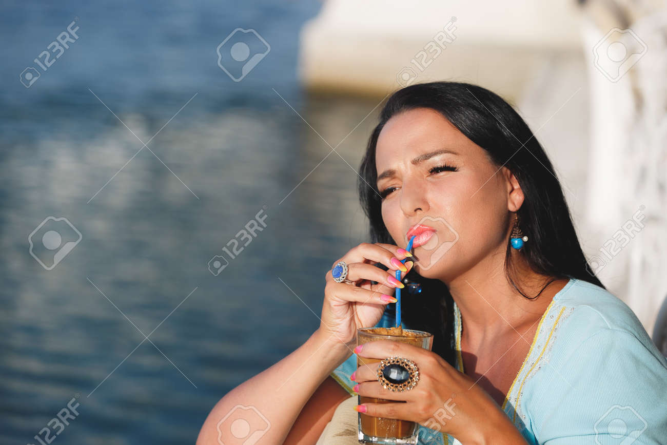 Happy Tanned Woman Drinking Iced Coffee In Seaside Cafe During Sunset Selective Focus Copy Happy Tanned Woman Drinking Iced Coffee In Seaside Cafe During Sunset Selective Focus Copy
