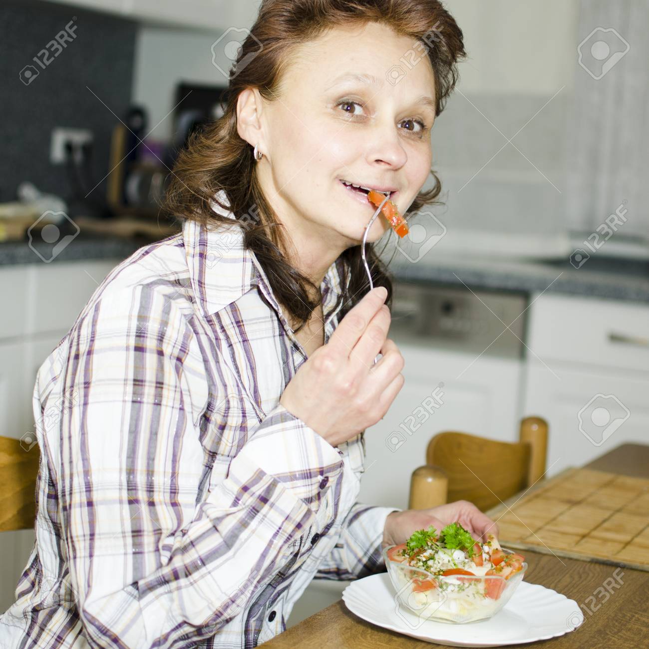 A woman is eating salad in the kitchen. - 17079591 A woman is eating salad in the kitchen. - 17079591