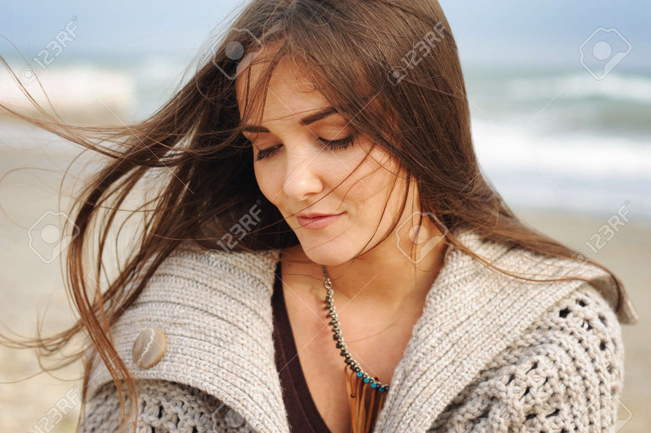 Beautiful young happy woman portrait against seascape, long hair fluttering in the wind, looking down, casual autumn fashion, healthy lifestyle - 67680810 Beautiful young happy woman portrait against seascape, long hair fluttering in the wind, looking down, casual autumn fashion, healthy lifestyle - 67680810