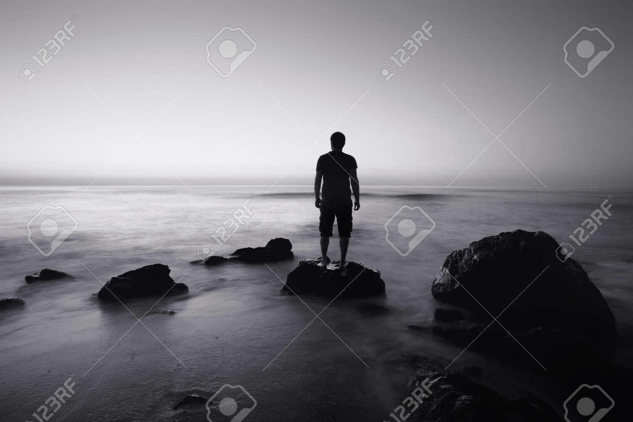 Black and white seascape with alone man on the rocks