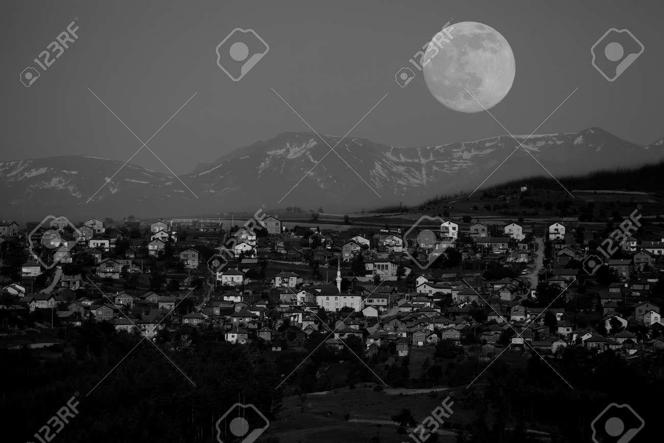 Unusual big moon over the small mountain village black and white