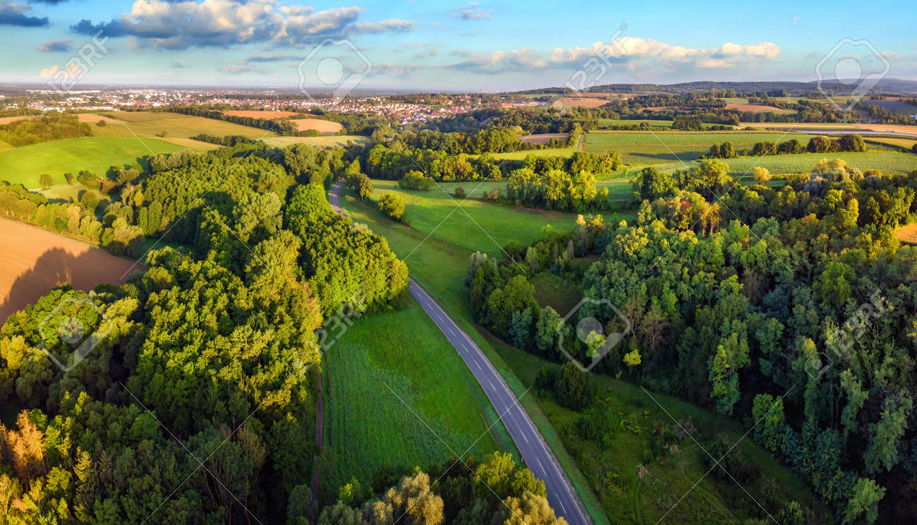 Idyllic German landscape shot from above in early morning sunlight: meadows and forests with blue sky and a road leading to a small town on the horizon - 149775554 Idyllic German landscape shot from above in early morning sunlight: meadows and forests with blue sky and a road leading to a small town on the horizon - 149775554