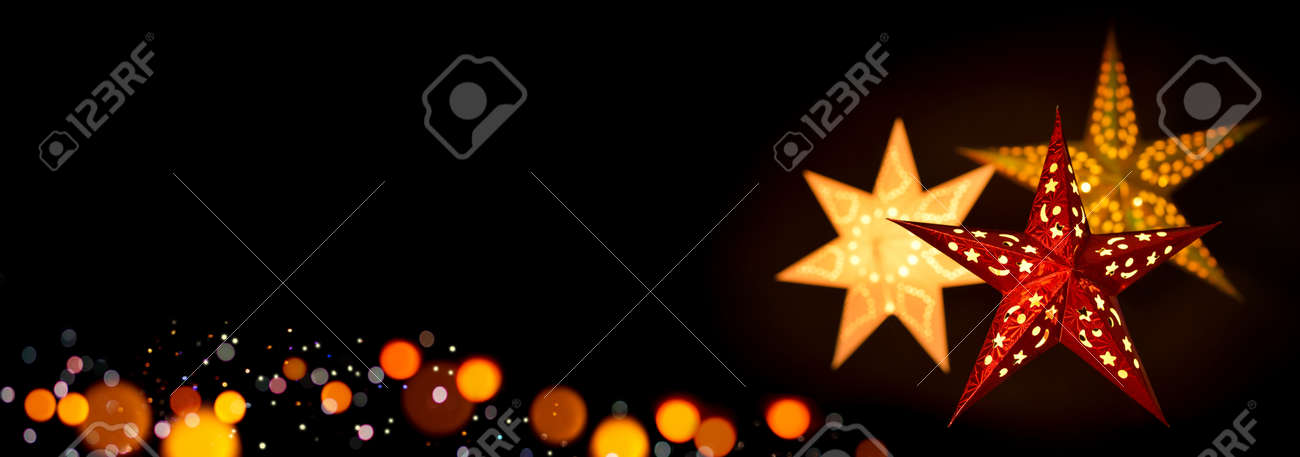 Shining red and gold Christmas star lanterns framing a simple, extra wide black background as copy space - 159388402 Shining red and gold Christmas star lanterns framing a simple, extra wide black background as copy space - 159388402