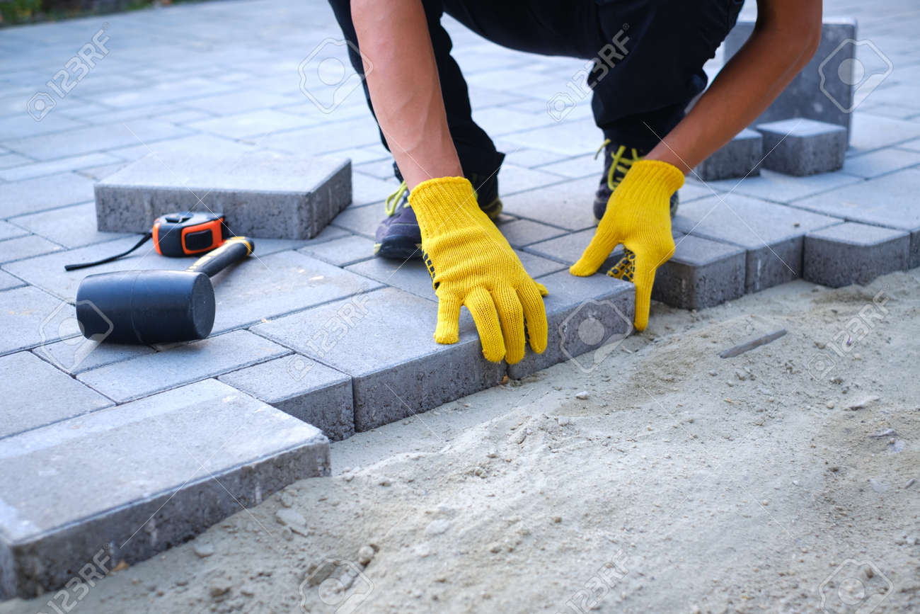 The Master In Yellow Gloves Lays Paving Stones In Layers Garden Brick Pathway Paving By Professional Paver Worker Laying Gray Concrete Paving Slabs In House Courtyard On Sand Foundation Base Stock Photo