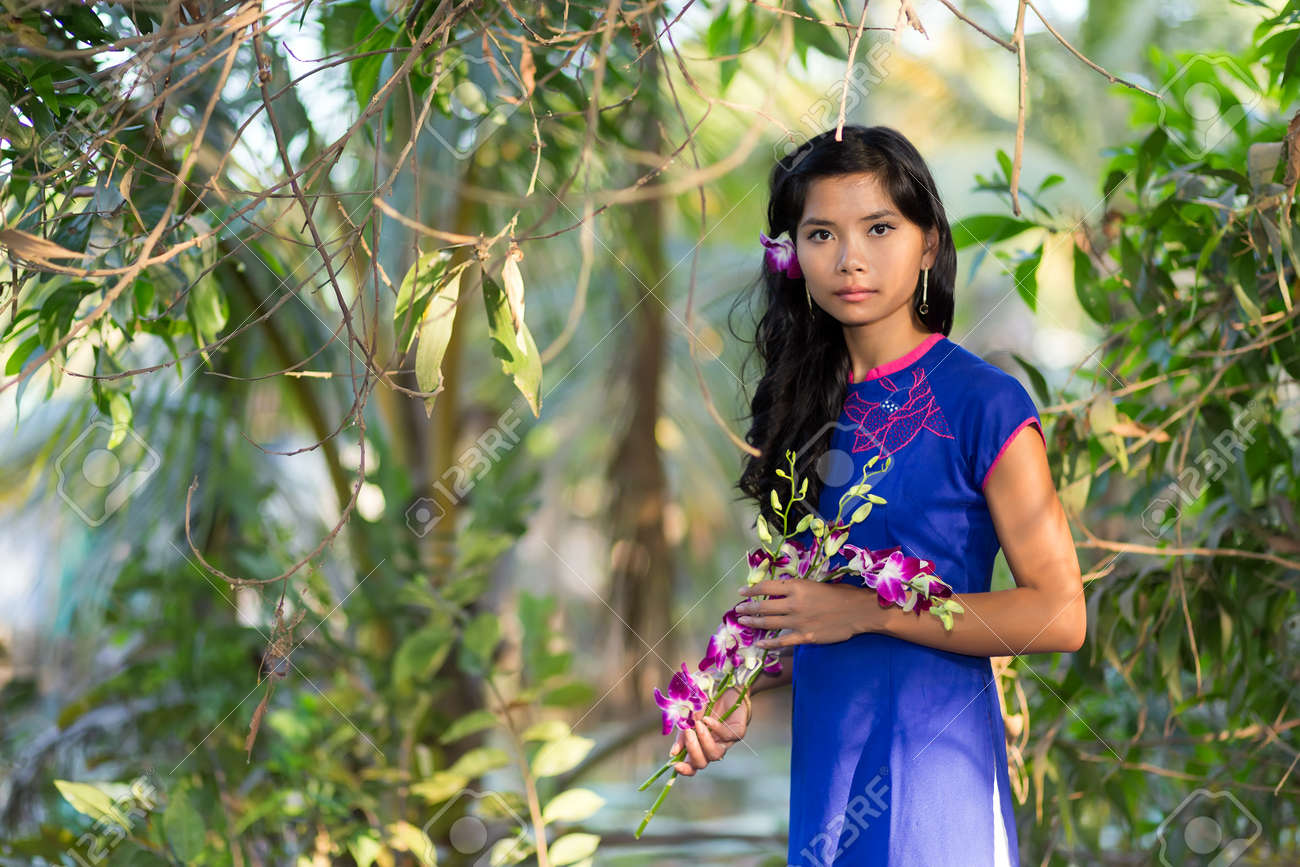 南国の花々 の持株スプレーに立っている彼女は緑豊かな緑の木々 の公園に立っているので豪華な若いベトナム人女性 の写真素材 画像素材 Image