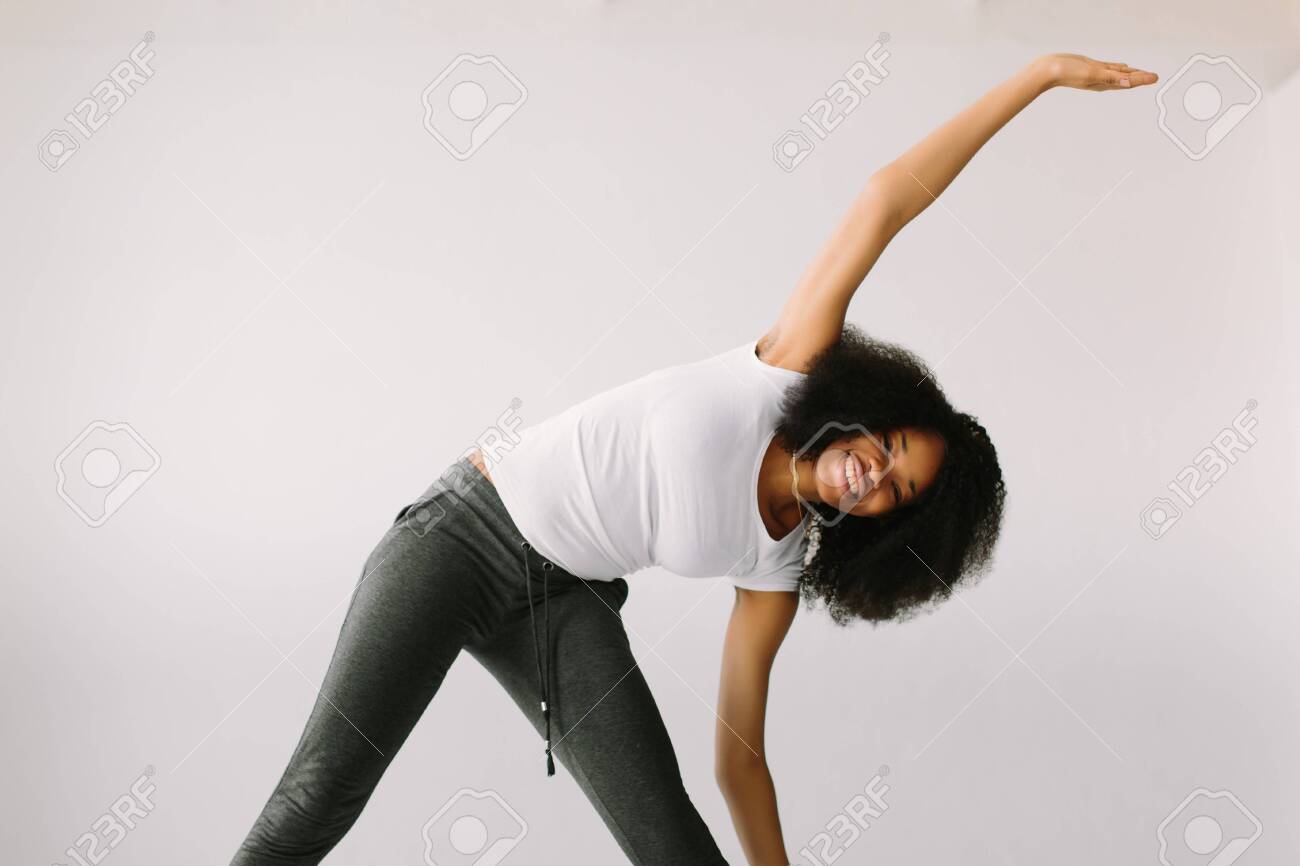 An African American young woman standing on a white bed and doing physical exercises - 147230795 An African American young woman standing on a white bed and doing physical exercises - 147230795