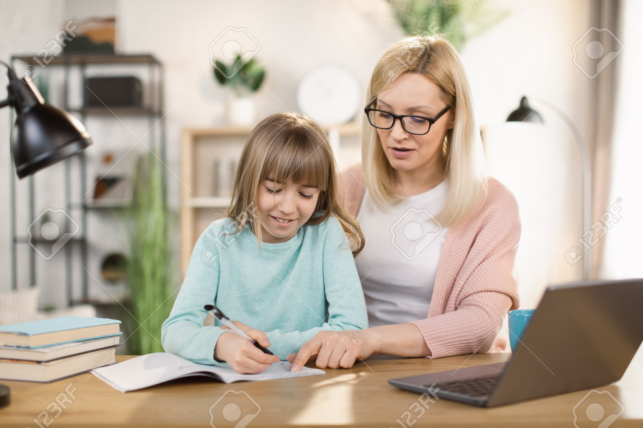 女子高生と婚約している白人の家庭教師は、自宅のテーブルに座ってタスクを完了するのに役立ちます。教育の子供の発達の概念、継母の概念で宿題を書くヨーロッパの子供のホームスクーリングの写真素材・画像素材  Image 184489352