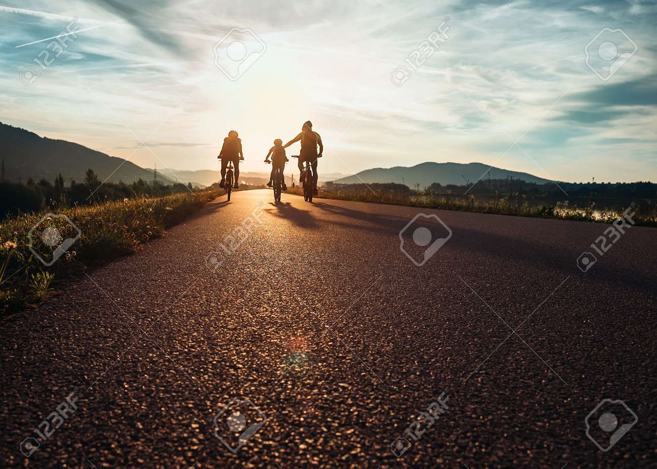 Сyclists family traveling on the road at sunset - 65053758 Сyclists family traveling on the road at sunset - 65053758