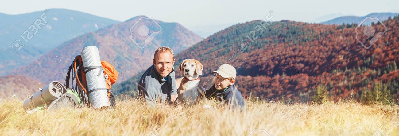 Father and son backpackers hikers rest on mountain hill with their beagle dog - 110717406 Father and son backpackers hikers rest on mountain hill with their beagle dog - 110717406