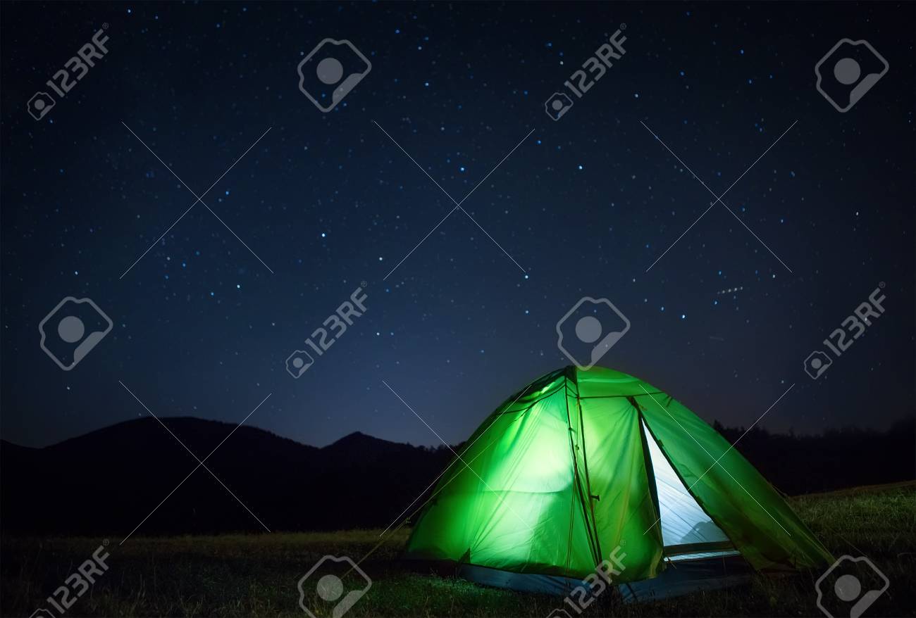 Camping tent with light inside is on the mountain valley under night starry sky - 112309200 Camping tent with light inside is on the mountain valley under night starry sky - 112309200