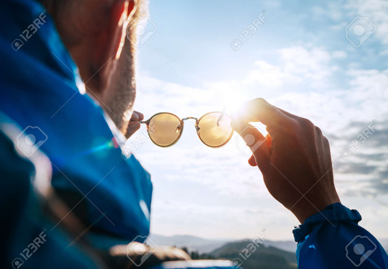 Backpacker man looking at bright sun through polarized sunglasses enjoying mountain landscape. - 130603213 Backpacker man looking at bright sun through polarized sunglasses enjoying mountain landscape. - 130603213