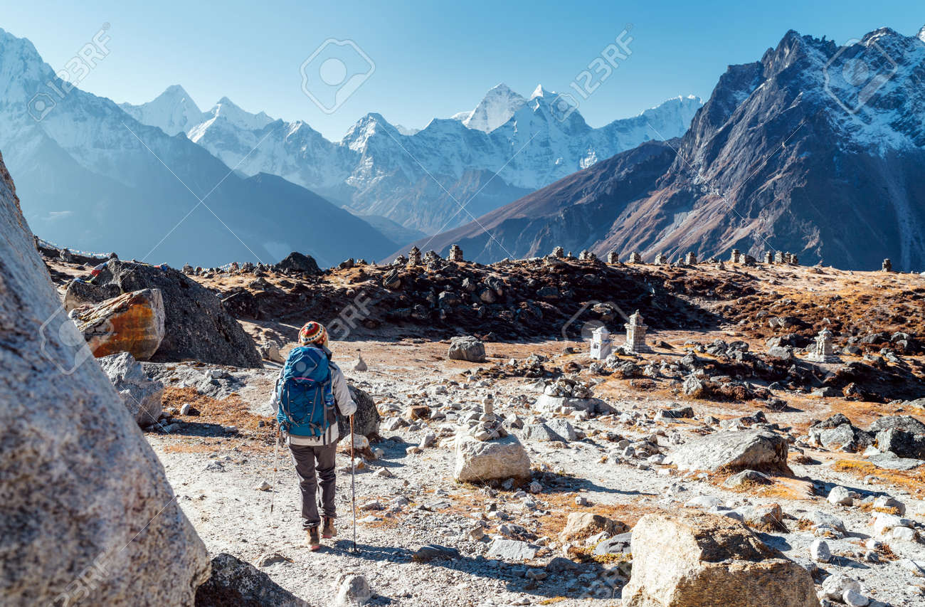 Junge rucksacktouristin, die der trekkingroute des everest base camp mit trekkingstöcken folgt und den blick auf das tal mit dem ama dablam-gipfel genießt. sie kam zum everest memorial to lost mountaineers (4800m) - 135506090 Junge rucksacktouristin, die der trekkingroute des everest base camp mit trekkingstöcken folgt und den blick auf das tal mit dem ama dablam-gipfel genießt. sie kam zum everest memorial to lost mountaineers (4800m) - 135506090