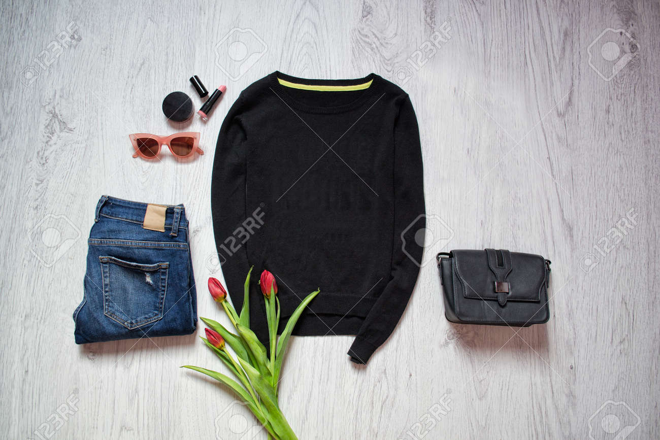 ファッションの概念 黒のセーター チューリップ ブルー ジーンズ 黒のバッグ サングラス 口紅 春のワードローブ 木製の背景 トップ ビュー の写真素材 画像素材 Image