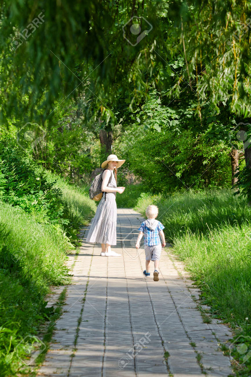 Mom And Son Walking Along The Road In The Park Back View