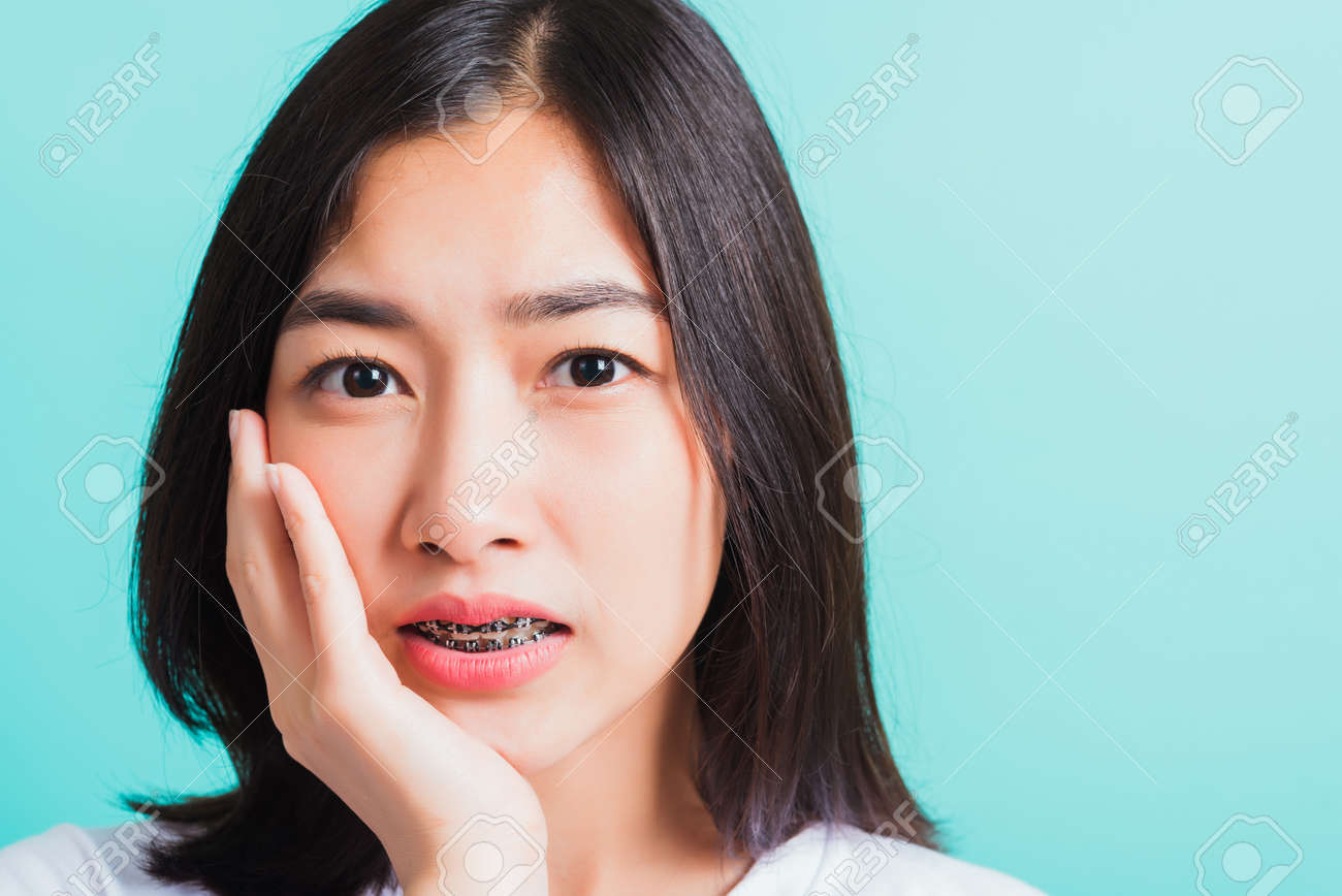 JC女性器接写 アジアの十代の美しい若い女性の笑顔の肖像画は、彼女の不幸な痛みの歯痛を笑って歯に歯列矯正器を持っており、青い背景、医学と歯科の概念で分離された手で頬に触れますの写真素材・画像素材  Image 156597500