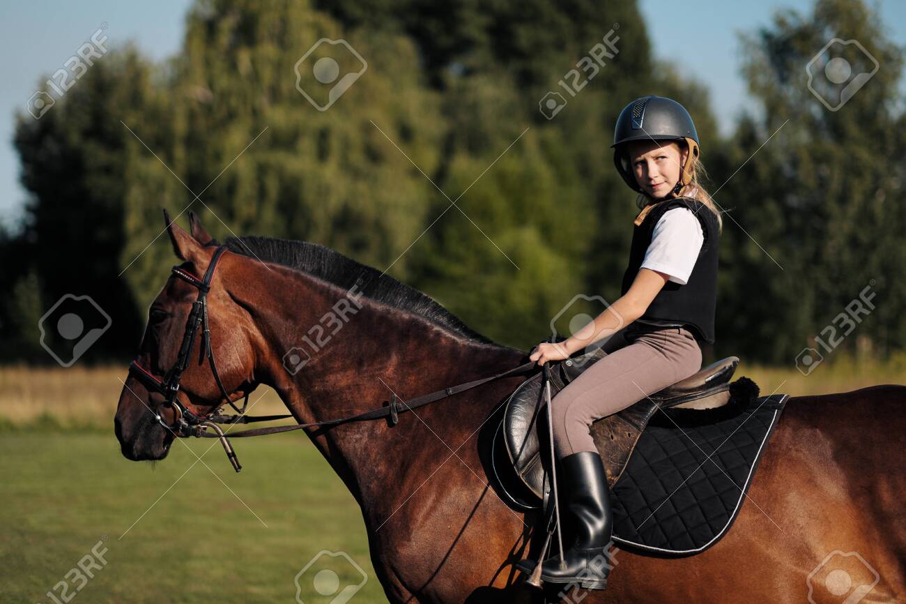 Girl teenager jockey sits on a brown horse in nature. Dressage horses, rider training. - 128929373 Girl teenager jockey sits on a brown horse in nature. Dressage horses, rider training. - 128929373