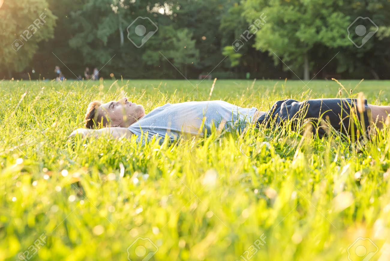 ハンサムな若い男は日没でのんびりと芝生で横になっています の写真素材 画像素材 Image