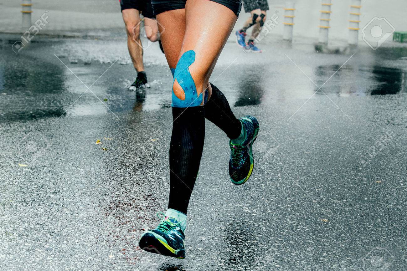 feet girl runners in compression socks and taping on his knees, running on wet asphalt - 61632028 feet girl runners in compression socks and taping on his knees, running on wet asphalt - 61632028