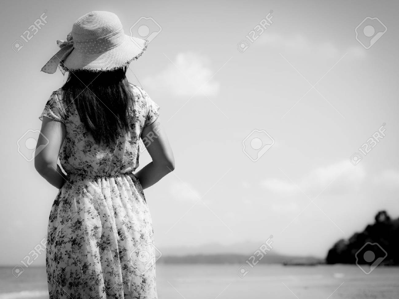 Black and white of sad woman in summer vacation wearing straw hat and beach dress looking