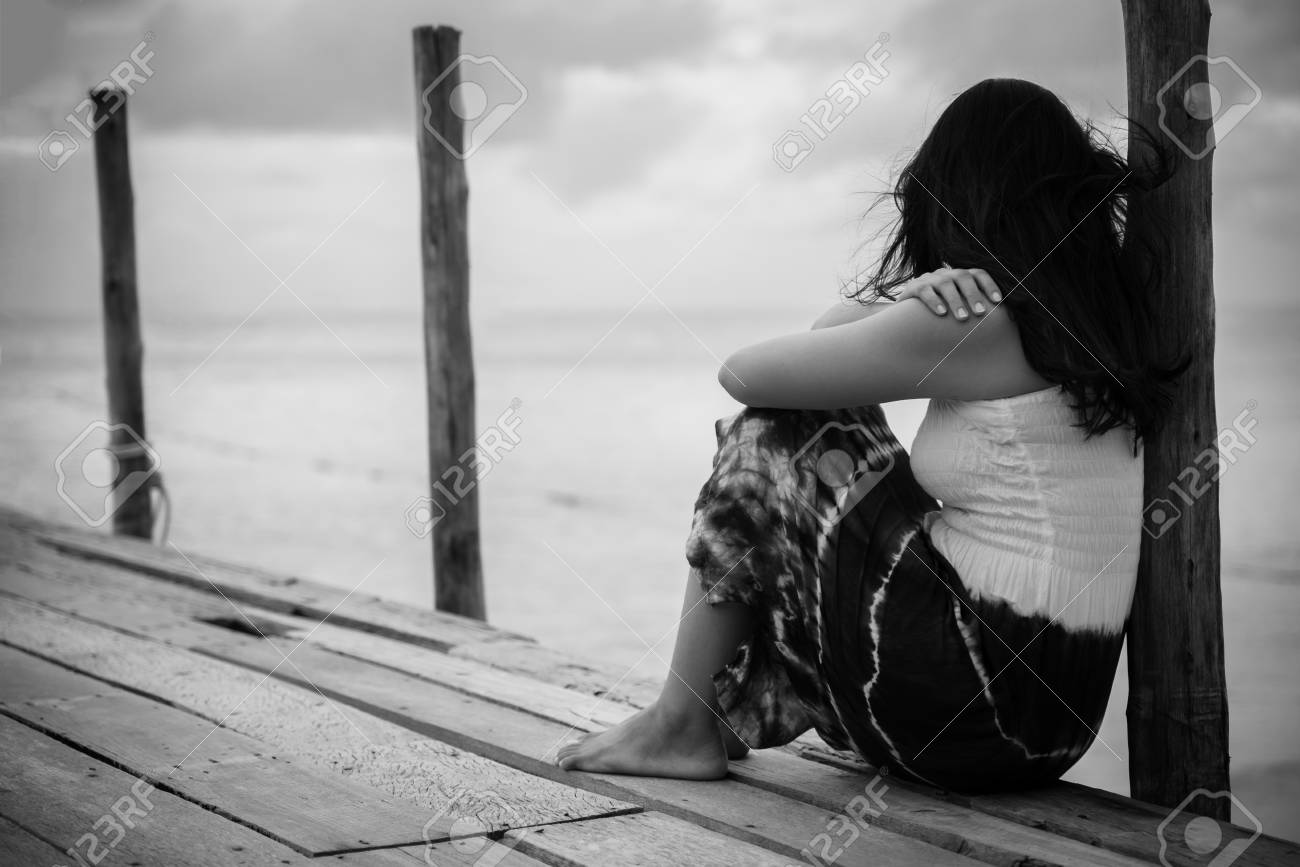 Black and white of sad and lonely woman sitting alone on a the wooden bridge over