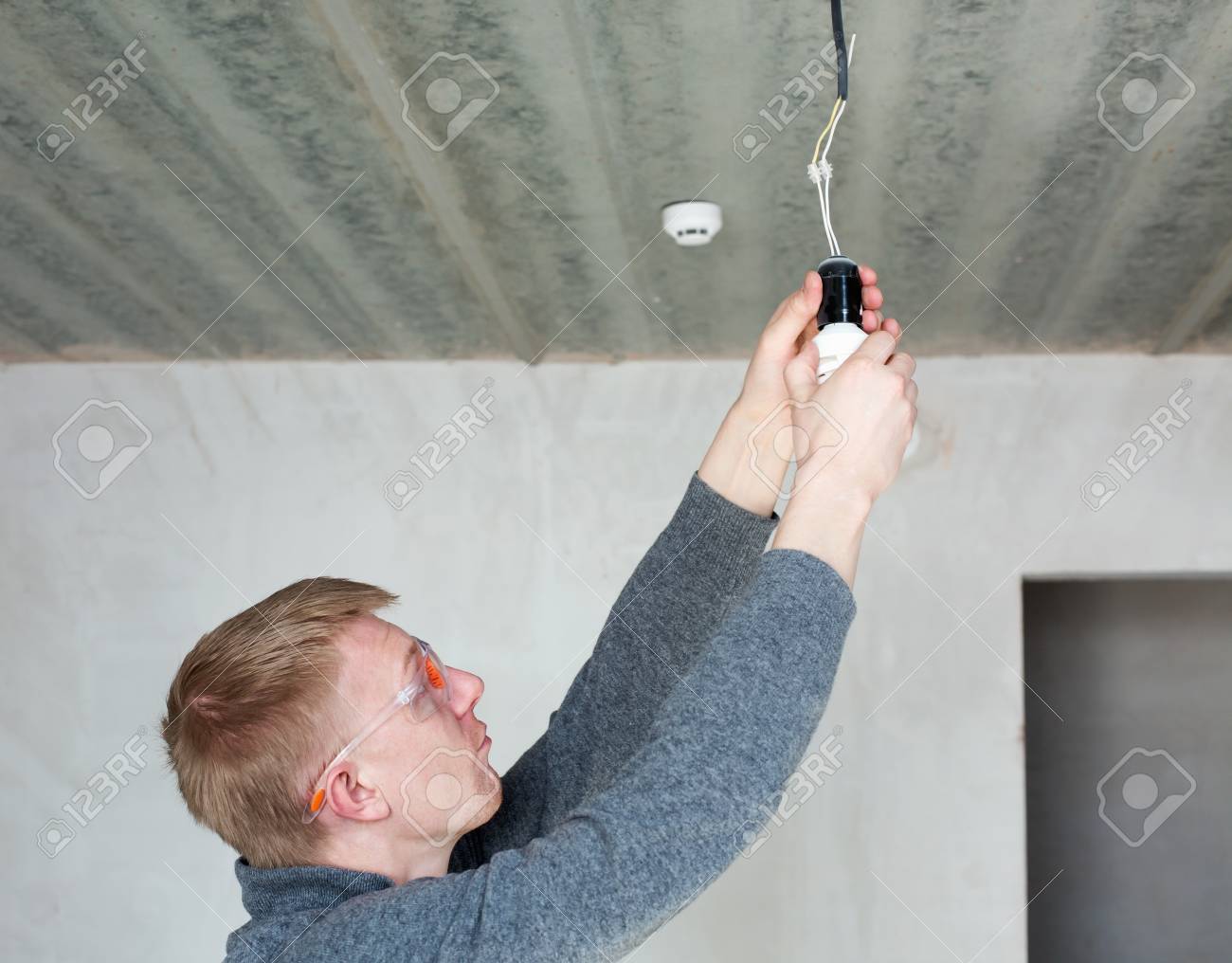 A man in safety glasses changing energy saving light bulbs - 47070189 A man in safety glasses changing energy saving light bulbs - 47070189
