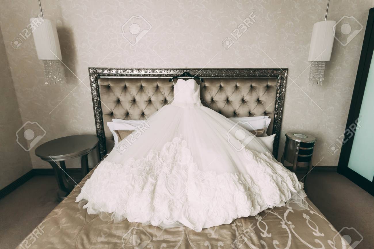 a cream and luxury bridal dress which lie on a bed in room indoor