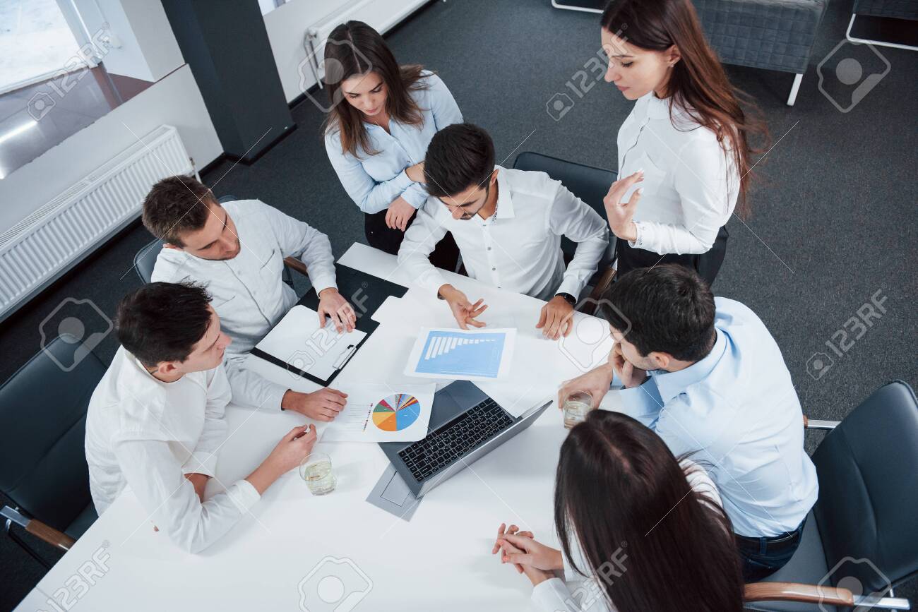 Top view of office workers in classic wear sitting near the table using laptop and documents. - 134794531 Top view of office workers in classic wear sitting near the table using laptop and documents. - 134794531