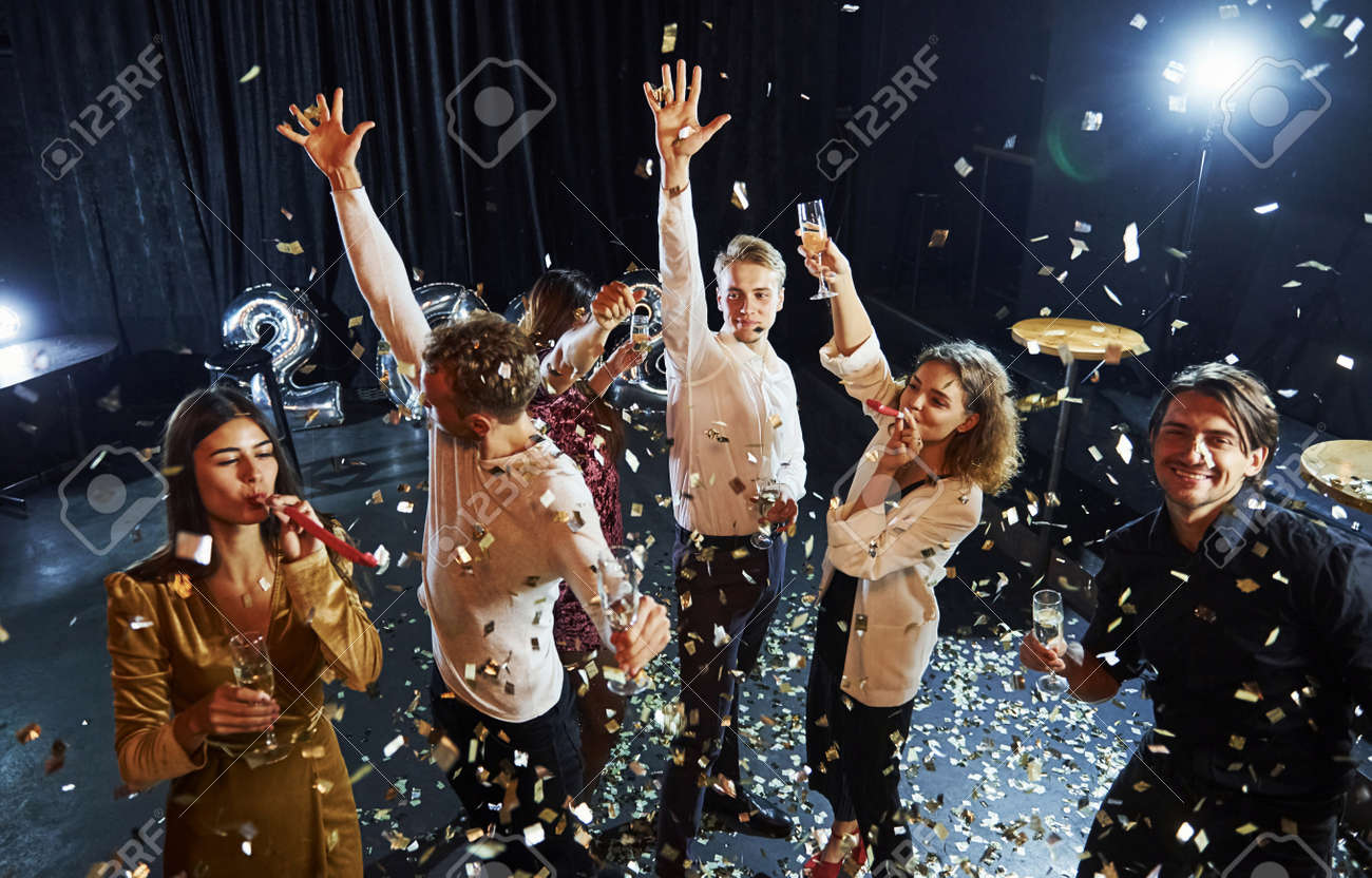 Confetti is in the air. Group of cheerful friends celebrating new year indoors with drinks in hands. - 157225221 Confetti is in the air. Group of cheerful friends celebrating new year indoors with drinks in hands. - 157225221
