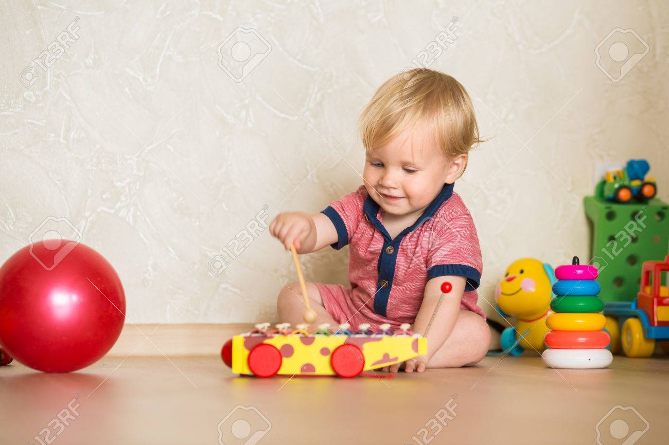 Retrato De Un Hermoso Bebé En El Suelo Con Los Juguetes. 1,5 Años De Edad, Niño Jugando Con Juguetes De La Taza De Educación En El Hogar. Poco Chico Rubio Con Ojos