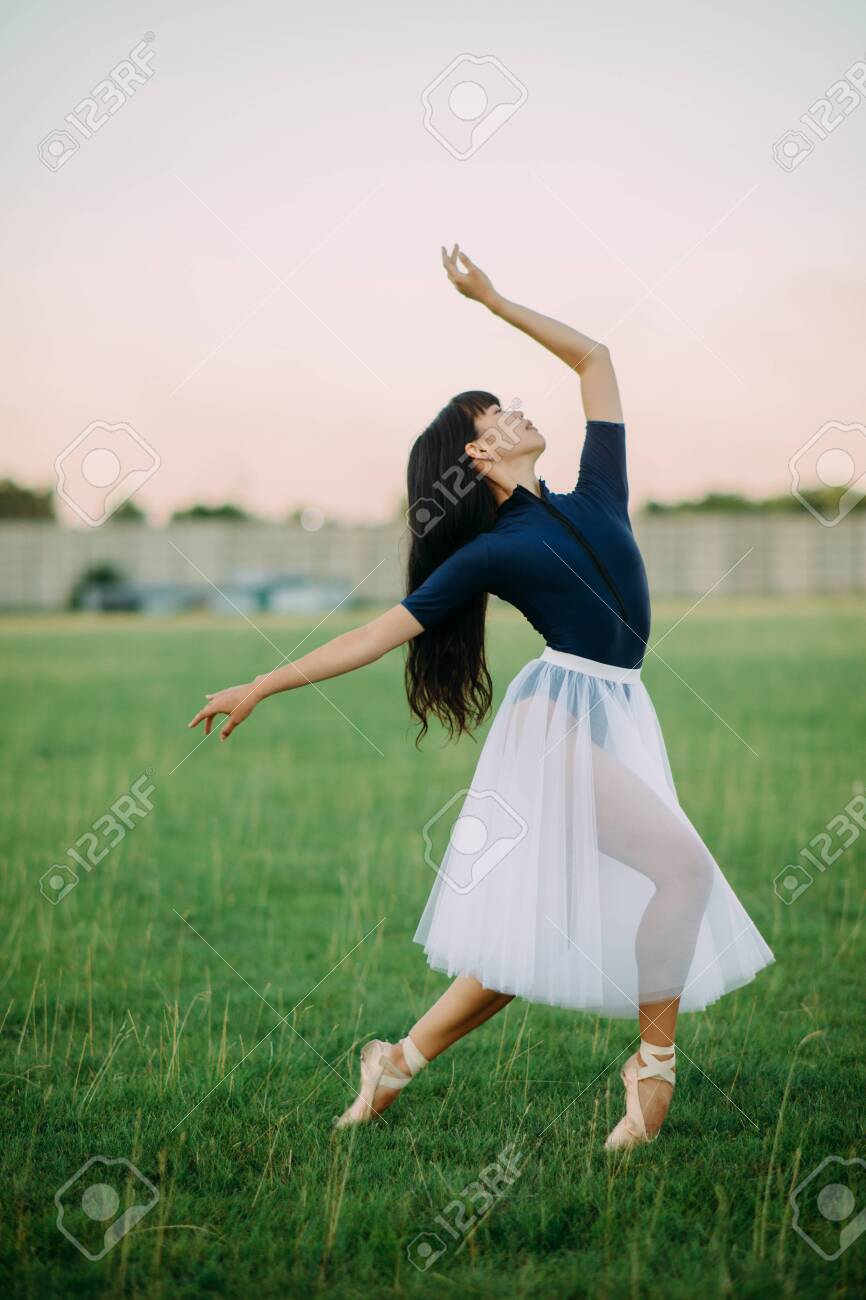 Japanese ballerina in white skirt dances on lawn background. 