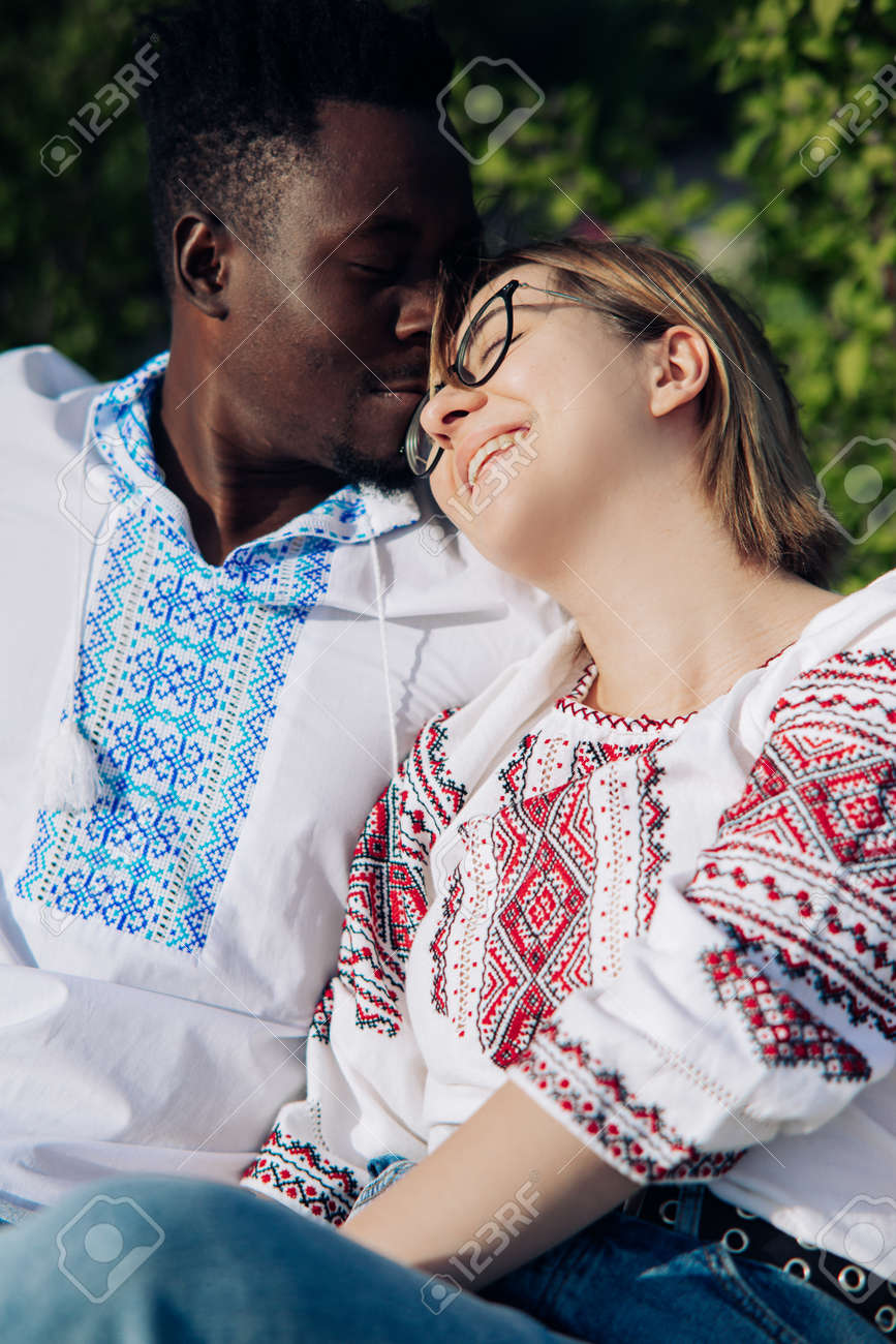Pareja Feliz Interracial Se Sienta En Un Banco En El Jardín Vestida Con Camisas Bordadas étnicas Ucranianas. Concepto De Relaciones De Y Unidad Entre Diferentes Humanas. Fotos, Retratos,