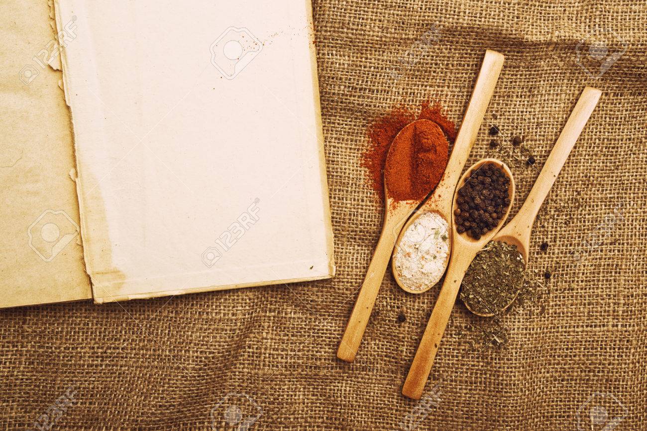 Kitchen Table With Food spices. food ingredients on wood spoons with open book on kitchen Kitchen Table With Food spices. food ingredients on wood spoons with open book on kitchen