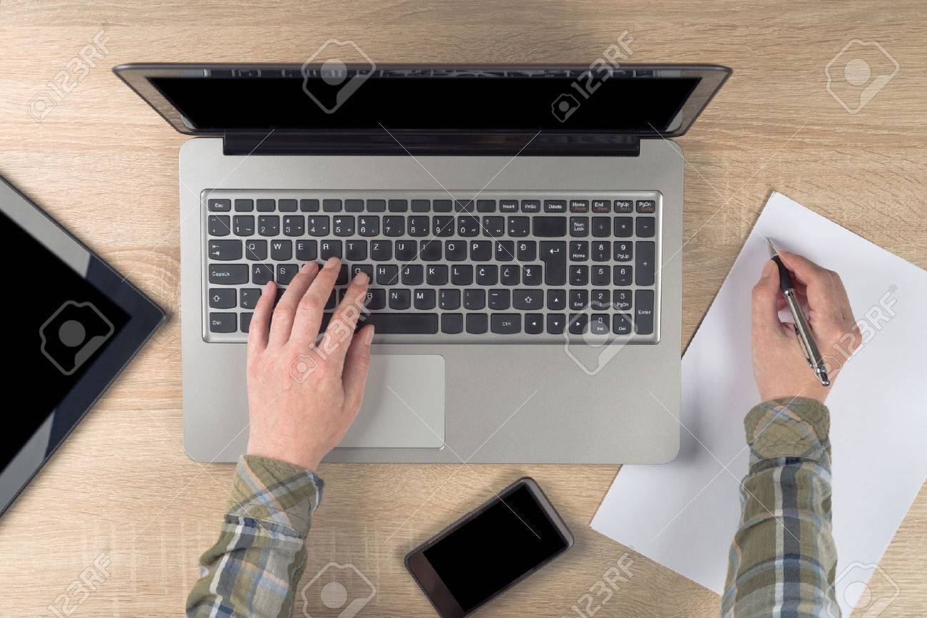 Female programmer writing notes on piece of paper while typing laptop keyboard, top view. - 31197867 Female programmer writing notes on piece of paper while typing laptop keyboard, top view. - 31197867