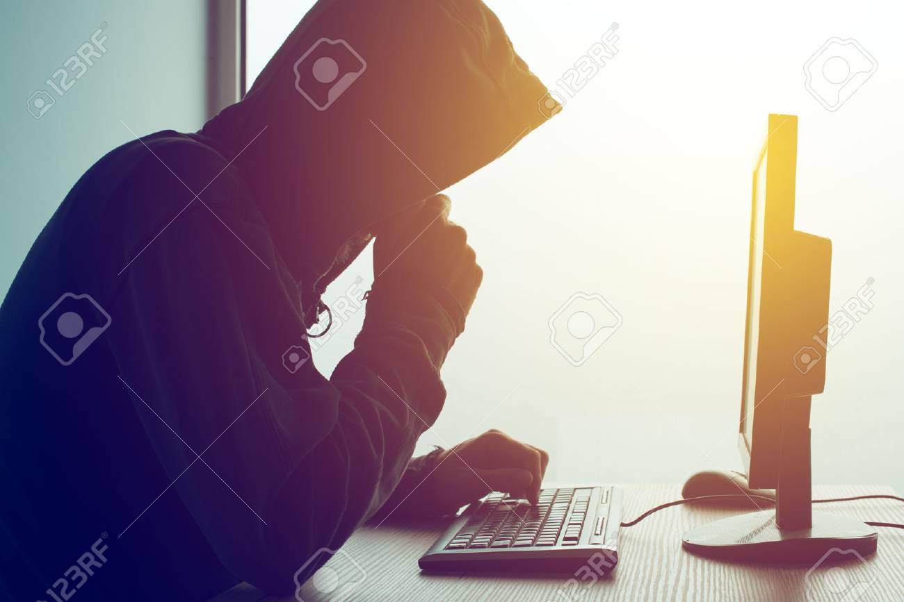Hooded computer hacker hacking network. Male with black hoodie using computer for identity theft or other criminal online activity. - 88188244 Hooded computer hacker hacking network. Male with black hoodie using computer for identity theft or other criminal online activity. - 88188244