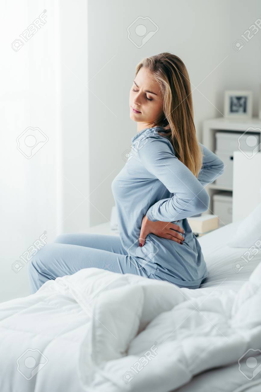 Young attractive woman with back pain waking up and sitting on her bed, she is touching her back - 67009189 Young attractive woman with back pain waking up and sitting on her bed, she is touching her back - 67009189