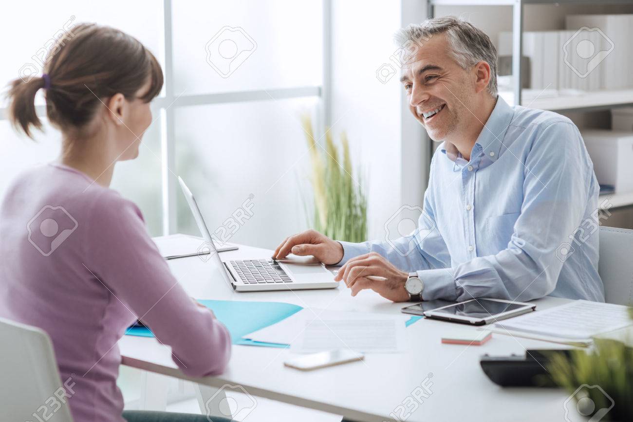 Confident advisor meeting with a customer in his office, he is explaining a contract document and policy to the woman sitting at his desk - 70830970 Confident advisor meeting with a customer in his office, he is explaining a contract document and policy to the woman sitting at his desk - 70830970