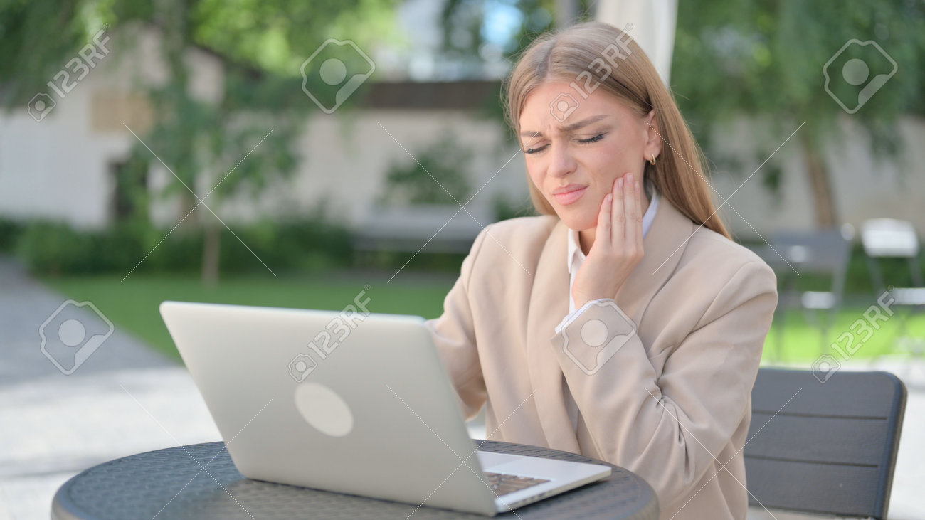 Businesswoman with Laptop having Toothache in Outdoor Cafe - 172195430 Businesswoman with Laptop having Toothache in Outdoor Cafe - 172195430