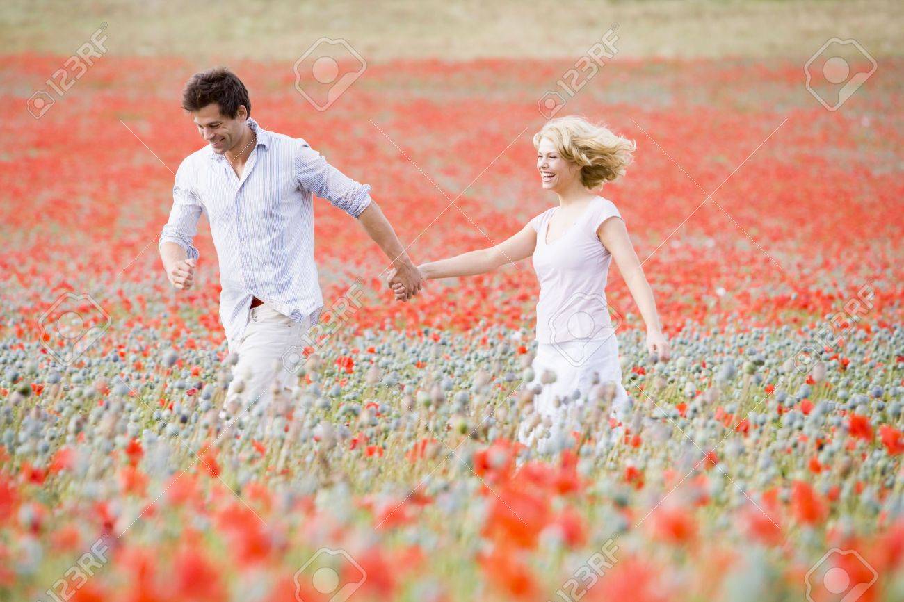 Couple walking in poppy field holding hands smiling - 3600150 Couple walking in poppy field holding hands smiling - 3600150
