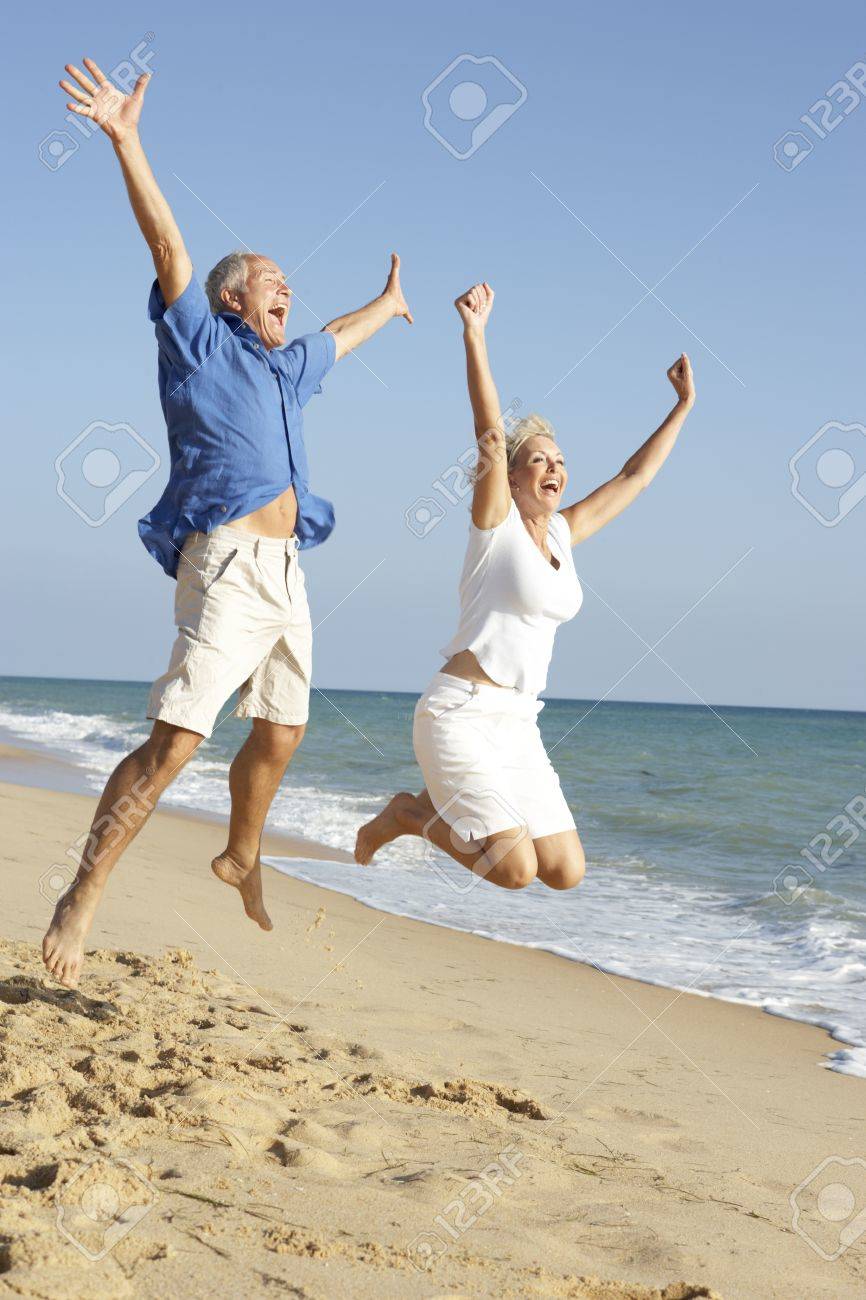 Senior Couple Enjoying Beach Holiday Jumping In Air - 65656177 Senior Couple Enjoying Beach Holiday Jumping In Air - 65656177