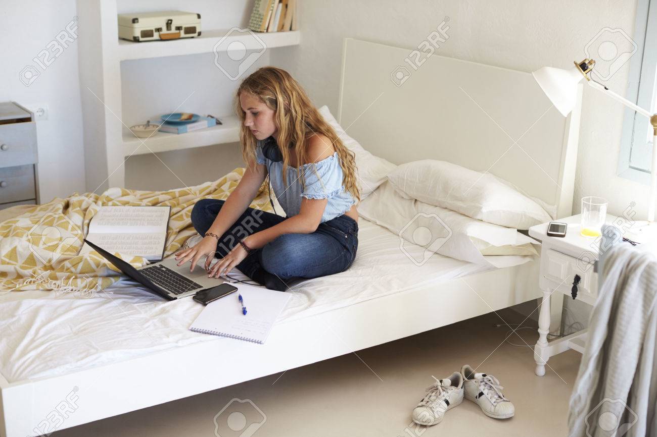 Girl using laptop for homework sitting cross legged on bed - 71403188 Girl using laptop for homework sitting cross legged on bed - 71403188