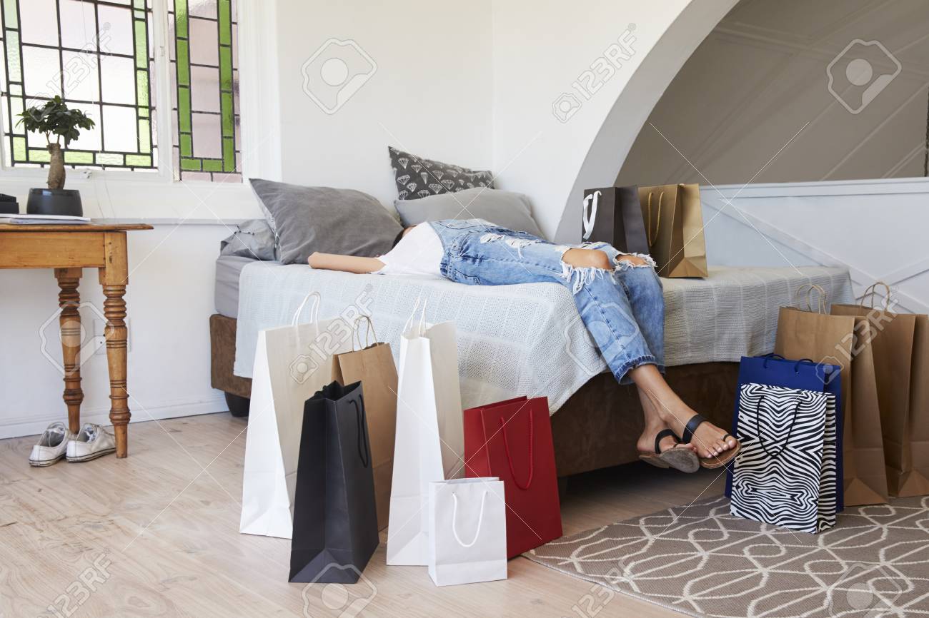 買い物袋に囲まれた旅行から戻って女性がベッドの上にあります の写真素材 画像素材 Image