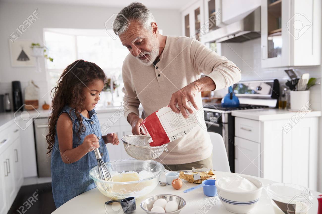 Young girl preparing cake mixture with her grandfather at the kitchen table, close up - 115390747 Young girl preparing cake mixture with her grandfather at the kitchen table, close up - 115390747