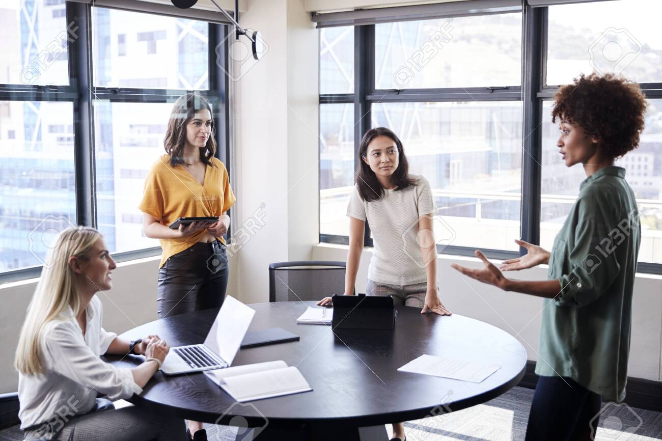 Female creatives in a meeting room listening to their colleague making an informal presentation - 122609314 Female creatives in a meeting room listening to their colleague making an informal presentation - 122609314