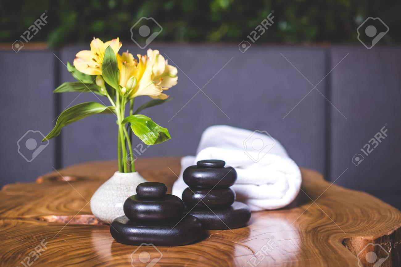 Yellow daffodils stand in a white vase. Pyramid of dark stones for massage close-up. Pyramids of stones for massage lie on the table. White towels lie in the background. - 94135533 Yellow daffodils stand in a white vase. Pyramid of dark stones for massage close-up. Pyramids of stones for massage lie on the table. White towels lie in the background. - 94135533