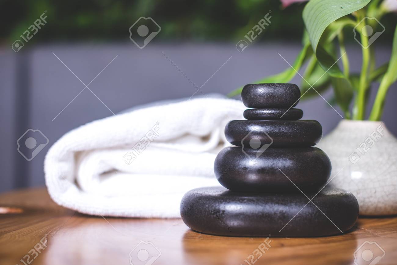 Close-up on dark stones for massage on a wooden table. White towels lie in the background. - 94135537 Close-up on dark stones for massage on a wooden table. White towels lie in the background. - 94135537
